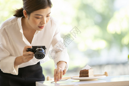 拿着相机拍甜品照片的年轻女子图片