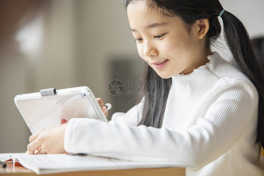小女孩坐在课桌上使用平板电脑学习图片