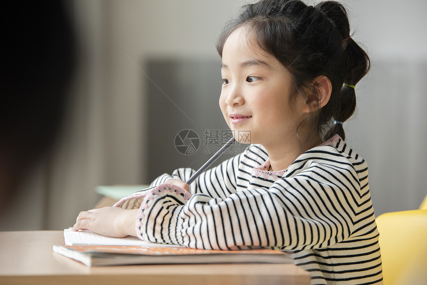 小女孩坐在课桌上认真写作业图片