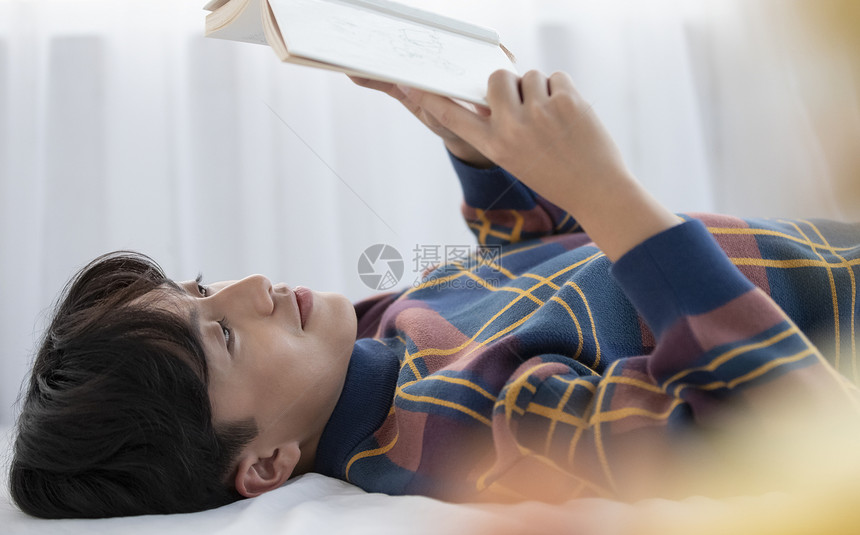 阅读泛亚洲阅读器在他的房间里读书的年轻人图片