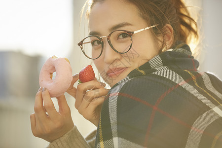 吃甜甜圈女孩拿着甜甜圈和草莓微笑的年轻女子背景