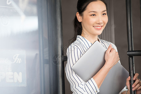 抱着笔记本电脑微笑的商务女性餐厅高清图片素材