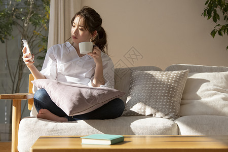 沙发上喝咖啡玩手机的年轻女子图片