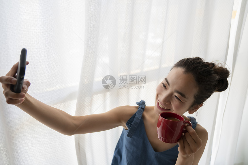 窗边拿着咖啡自拍的青年女性图片