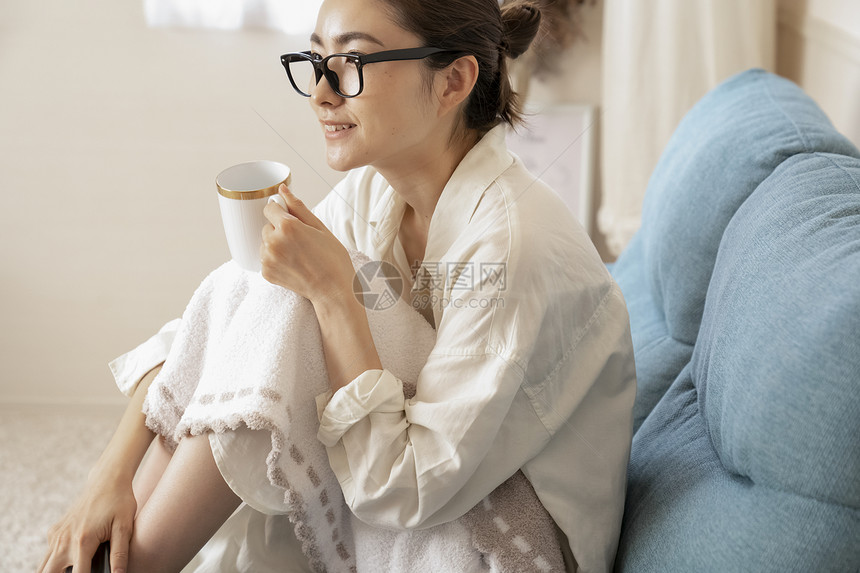 沙发上看电视拿着水杯的年轻女子图片