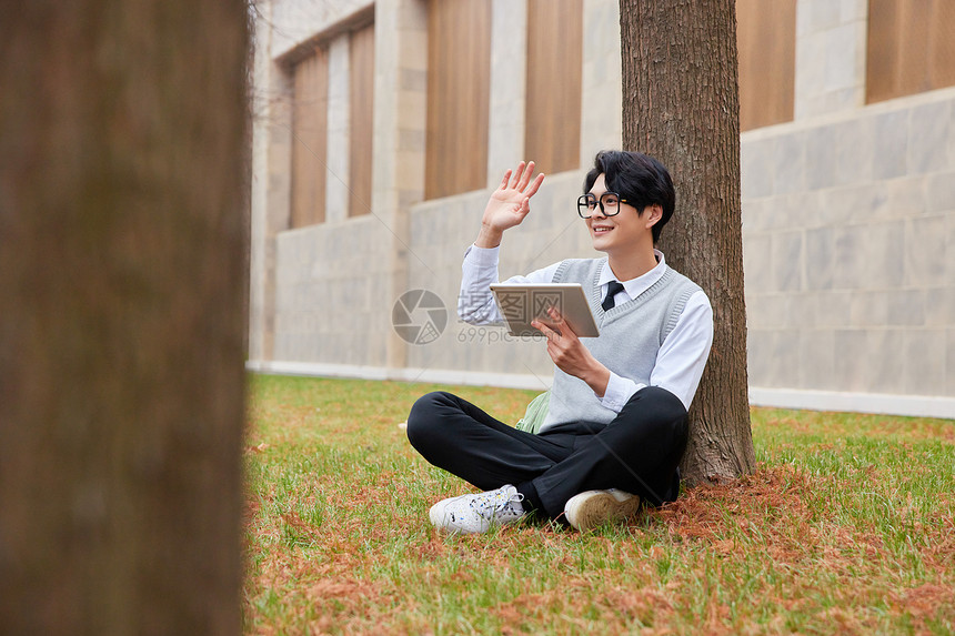 青年男性学生坐草地上打招呼图片