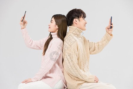 韩系情侣背靠背看手机背景图片