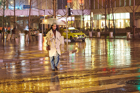下雨夜晚撑伞过马路的女性图片