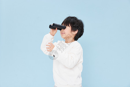 小男孩拿望远镜向远处看背景图片