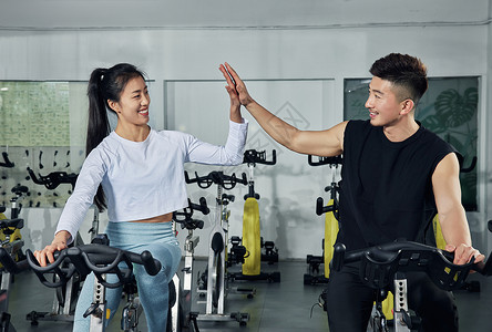 健身房动感单车训练的健身男女击掌鼓励背景图片