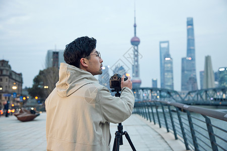 青年男摄影师使用三脚架拍摄城市风光照图片