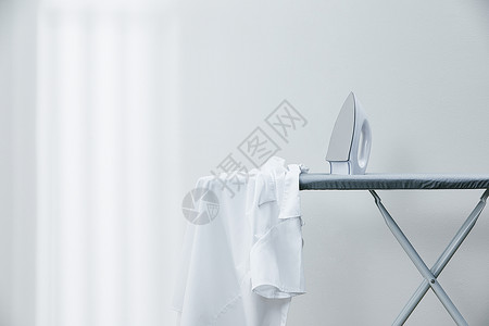 晾晒衣物烫衣板上放着的白衬衫和熨斗背景