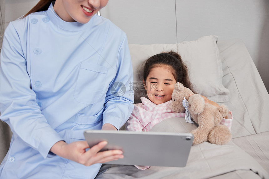 护士陪伴住院的小女孩看平板电脑特写图片