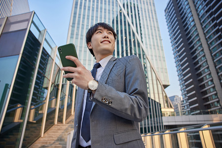 拿着手机仰望城市的商务男青年背景图片