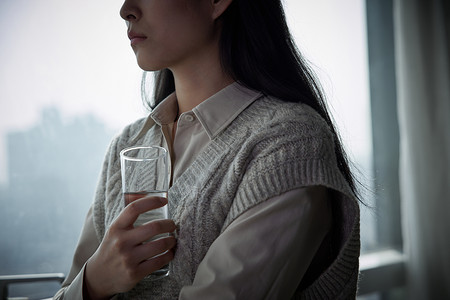 灰色心情窗边的独居女性手拿水杯背景