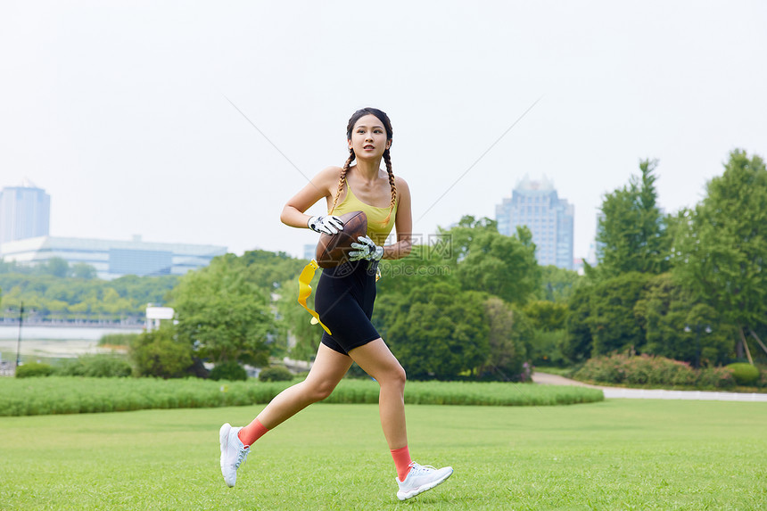 年轻美女抱着橄榄球奔跑图片