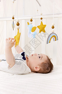 在婴儿床上玩摇铃的初生宝宝图片