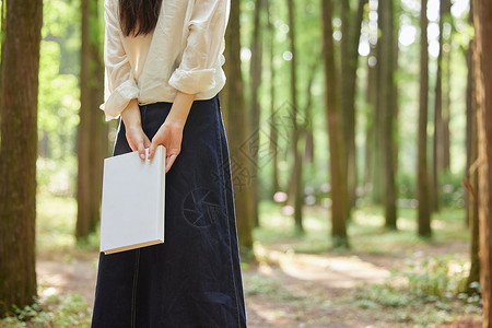 初秋女装促销在树林里手拿书本的美女背影背景