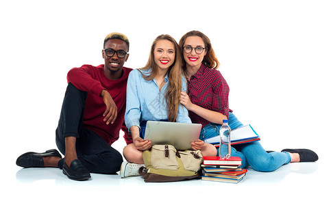 三名快乐的年轻青少年学生坐在书本笔记本电脑和白背景背景图片