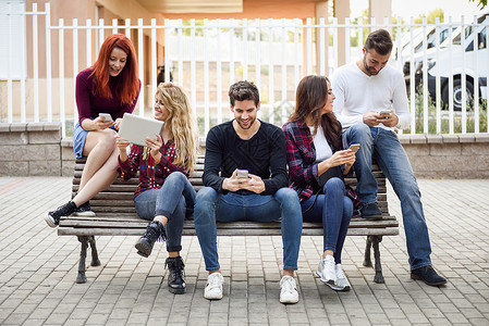 一群年轻人在户外长椅上使用智能手机和平板电脑图片