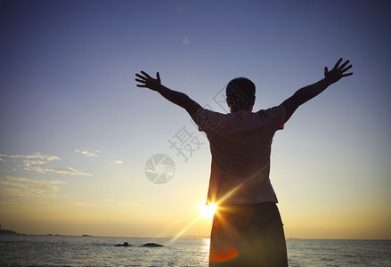 男子在日落时在举手或张开双臂的休图片