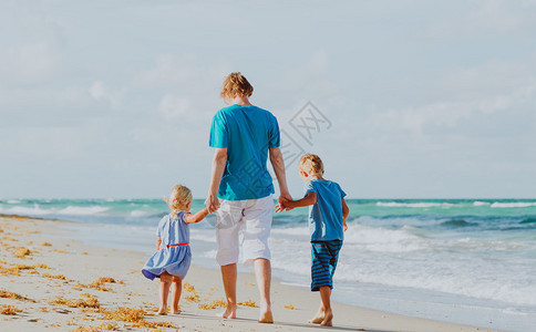 父亲和两个孩子在海滩上散步图片