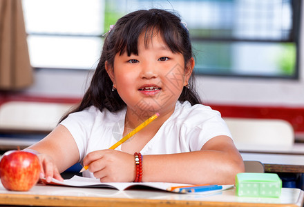 小学里漂亮的亚洲女孩在她的书上写字背景图片