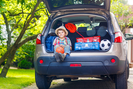 捕蝉小男孩可爱的小男孩在和父母一起去暑假前坐在汽车后备箱里带着手提箱和玩具去旅背景