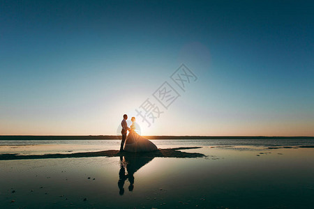 年轻的新娘和新郎身着长裙在海边的海岸线上的剪影图片
