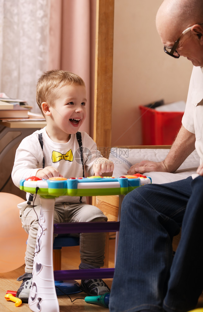 一个漂亮的笑着的小孩坐在卧室的一张小桌子旁和祖父玩耍的图片