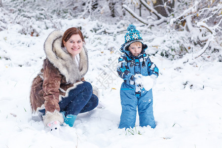 有趣的小男孩和他的妈在公园里玩第一场雪图片素材