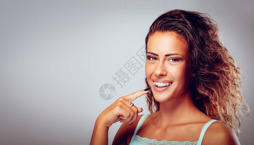微笑的年轻女人用牙套露出完美的白牙看着图片