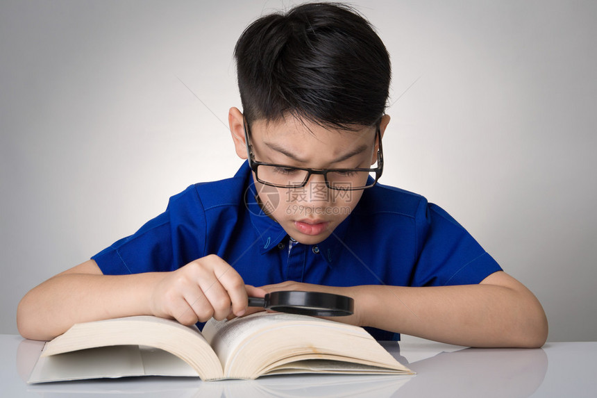 小亚洲男孩在灰色背景上读了一本由放图片