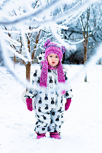 穿白色雪衣和粉红色帽子的女婴在雪地冬季公园穿图片