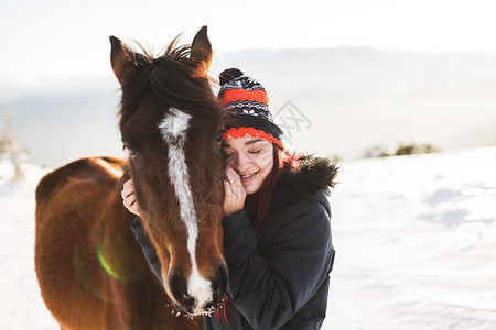快乐的女孩在闪亮的阳光下轻抚摸着马山中的冬天图片