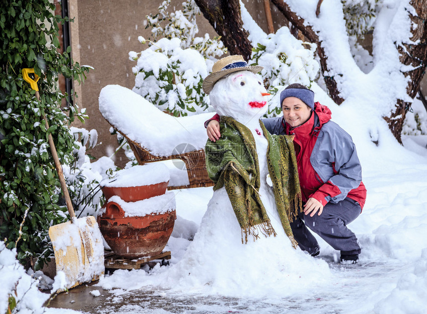 暴风雪期间一位女士在自家前院与雪人合影图片
