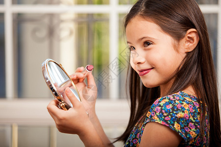 小女孩试着用小镜子画她的嘴唇背景图片