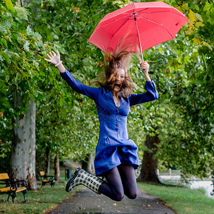 撑着红伞在雨中跳跃的幸福女人图片