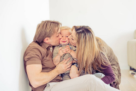 幸福的家庭和他们的小宝坐在地板上一家人在家里陪儿子亲吻他们图片