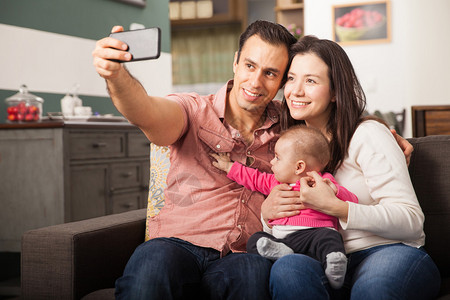 快乐的拉丁情侣在家中用智能手机自拍图片