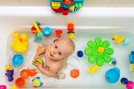 在浴缸里玩五颜六色的玩具微笑的小孩在浴室里看着相机婴儿玩耍图片