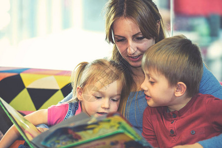 在儿童游戏室与两个孩子一起读童话故事的年轻漂亮图片
