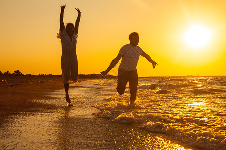 日落时在沙滩上奔跑的幸福情侣图片