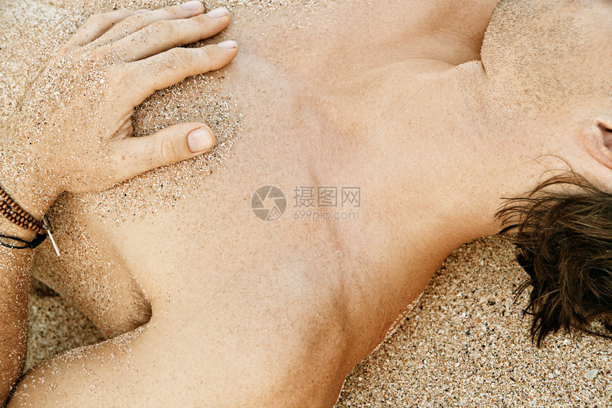 一个男人在金沙滩上晒太阳皮肤上有沙粒图片