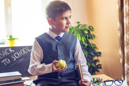 回到学校可爱的孩子坐在教室的课桌前男孩在放学时吃苹果小学图片