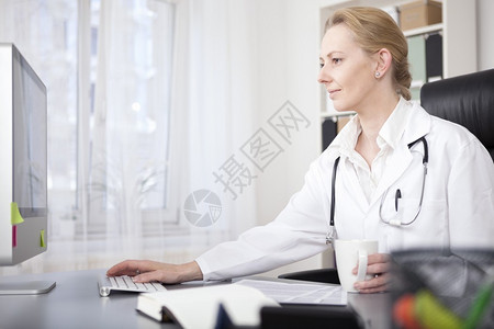 微笑的成年女医师在她的办公室一边喝着酒一边用图片
