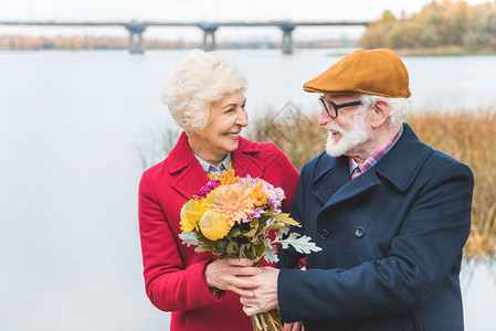 幸福的老夫妇站在秋天的湖边捧着一束鲜花图片