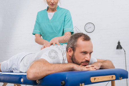 女按摩治疗师在诊所按摩桌上对病人进行按摩的局部图片