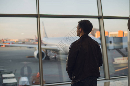 年轻人站在机场的窗户旁边图片