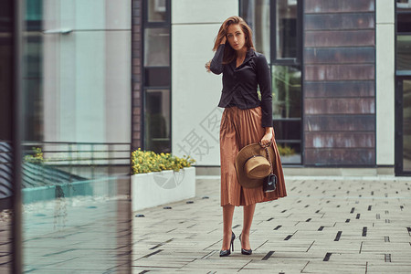 穿着黑色夹克棕色帽子和裙子的时装优雅女人带着手提包紧握在欧背景图片